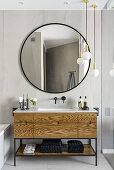 Bathroom in light grey, large round mirror, bathroom vanity covered in oak veneer