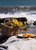 Glass with white wine on stone stools against blue sea and waves, summer picnic concept
