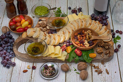Appetizer board with bread, cheese, nuts, olive oil, tomatoes and grapes