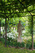 Pergola overgrown with vines, statue and snowball hydrangea in the garden