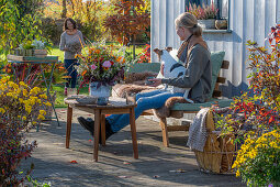 Zwei Frauen auf herbstlicher Terrasse mit Hund und Blumendekoration