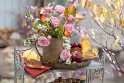 Herbstlicher Blumenstrauß aus Schneebeere (Symphoricarpos), Rosen und Herbstlaub auf Regal