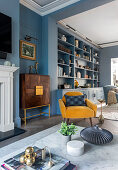 Blue built-in shelving unit, elegant highboard and yellow armchair in a living room