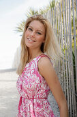 Blonde Frau in rosa-weißem Sommerkleid am Strand