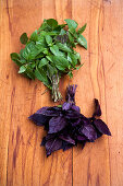 Green basil and red basil, one bunch each on a wooden background