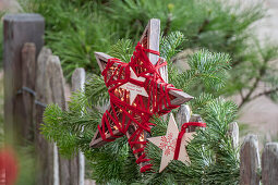 Holzsterne auf Tannenzweig an Gartenzaun, Weihnachtsdeko