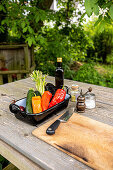 Frisches Gemüse, Gewürze, Messer und Holzbrett auf Gartentisch