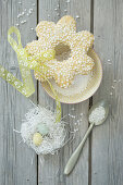 Blütenförmiges Osterplätzchen mit Hagelzucker, Nestchen mit weißem Ostergras und Zuckereiern