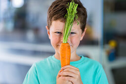 Boy in turquoise blue T-shirt with carrot at the table