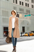 Young woman with glasses and a bag in a light coat on the street