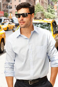 Junger Mann mit Sonnenbrille in hellem Hemd steht auf der Straße