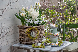 Narcissus 'Bridal Crown' (Narcissus), hyacinths (Hyacinthus), horned violets (Viola Cornuta) in a flower basket with a tiered arrangement of jugs and candy Easter eggs