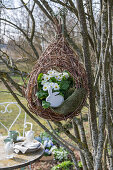 Wicker hanging basket planted with primroses (Primula) and Easter bunny in front of garden table
