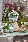 Tiered flower pots of horned violets and daisies, Easter eggs in egg carton decorated with feathers and Easter greetings on patio table