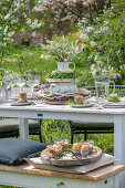 Gedeckter Tisch im Garten für Osterfrühstück mit Osternest und gefärbten Eiern in Eierbechern und Blumenstrauß in Etagere