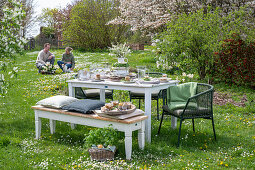 Young couple with dog sitting behind laid table Easter breakfast table with Easter nest and colored eggs in egg cups and parsley in basket in garden