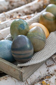 Easter eggs coloured with natural dyes in a wooden box with knitted doilies on birch branches
