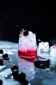 Refreshing summer drink with cherry and thyme sprig on ice