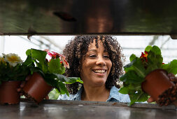 Lächelnde junge Frau in Gärtnerei begutachtet Blumentöpfe