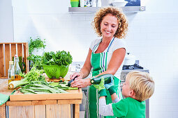Frau schneidet grünes Gemüse und Salat mit ihrem Sohn in der Küche zu