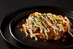 Okonomiyaki-Omelett nach japanischer Art, garniert mit Okonomi-Sauce, japanischer Mayonnaise und Frühlingszwiebeln
