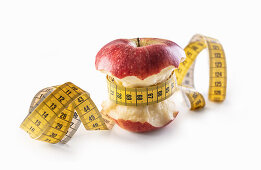 Red apple wrapped with measuring tape on a white background