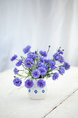 Bouquet of cornflowers (Centaurea cyanus) in white jug vase on table