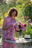 Woman at garden table and colourful bouquet of dahlias (Dahlia), roses (Rosa), autumn anemones (Anemone Hupehensis) and wild carrot