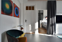 Living room in old building with designer armchair, artwork and view into the bedroom