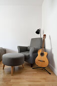 Grey armchair with stool and guitar in the corner of the room