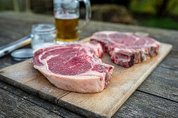Ox chops for grilling next to beer and grill tongs