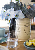 Orchideen und Eukalyptuszweige in Vase auf Tisch