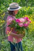 Frau mit Strauß aus Pfingstrosen (Paeonia) im Garten