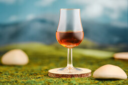 Glass of whisky on a mossy surface against a blurred mountain backdrop