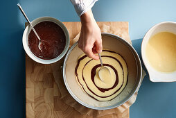 Making zebra cakes - alternate spoonfuls of light and dark batter into the centre of the baking tin