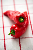 Two red pointed peppers on a chequered cloth