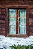 Fenster mit gemusterten Vorhängen im Holzhaus