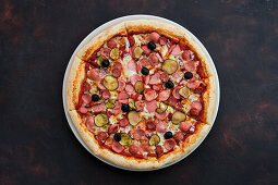 Pizza with various types of sausage, gherkins, olives and onions