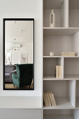 Wall mirror next to bookshelf reflects green armchair and grey sofa