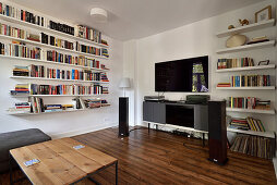 Living room with bookshelves, wooden floorboards and modern media furniture