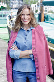 Junge Frau im Jeans-Outfit und rosa Strickjacke am Hafen