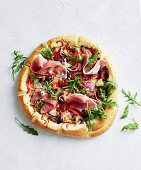 Pizza with prosciutto, rocket, onions and olives