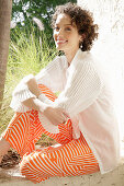 Brunette woman in cream-coloured blouse and orange-coloured patterned trousers