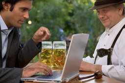 Old Bavarian man and young businessman with laptop in beer garden, Lake Starnberg, Bavaria, Germany
