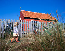 Little girl walking along fence and small house, Bornholm, Baltic Sea, Denmark