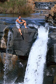 Mann sitzt auf Felsen neben einem Wasserfall, Mpumalanga, Südafrika