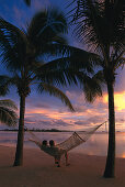 Paar entspannt sich in der Hängematte beim Sonnenuntergang, Aitutaki Lagoon Resort, Cook Islands, Südsee