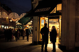 Menschen vor einem beleuchteten Geschäft am Abend, Regent Street, London, England, Grossbritannien, Europa