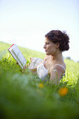 Junge Frau liegt in der Wiese und liest ein Buch