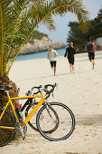 Three people on a cycle tour on the beach at cala santanyi, Majorca, Balearic Islands, Spain